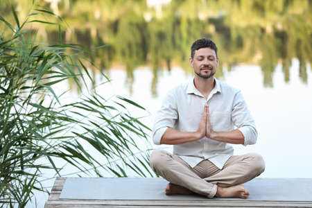 Man meditating on wooden pier near river. Space for textの写真素材