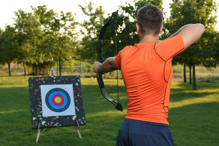 Man with bow and arrow aiming at archery target in park, back viewの写真素材