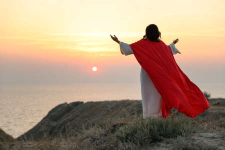 Jesus Christ raising hands on hills at sunset, back view. Space for textの写真素材
