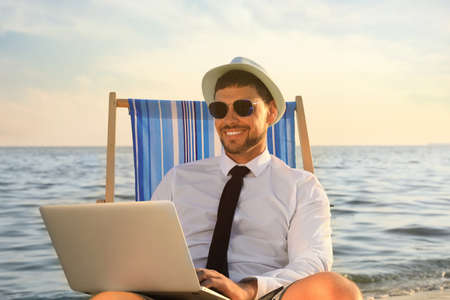Happy man with laptop on deckchair near sea. Business tripの写真素材