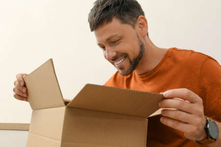 Happy man opening parcel indoors. Internet shoppingの写真素材