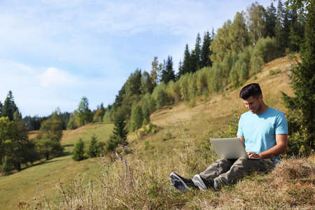 Man working with laptop outdoors surrounded by beautiful nature. Space for textの写真素材