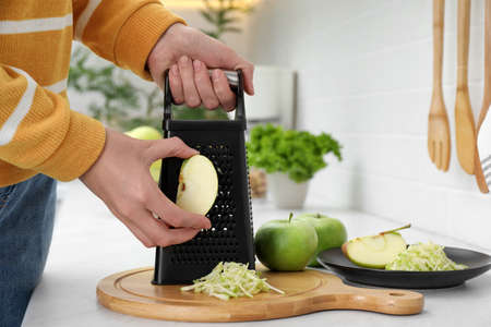 Woman grating fresh green apple at kitchen counter, closeup