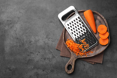 Grater and fresh ripe carrot on gray table, top view. Space for textの写真素材