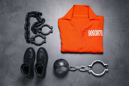 Prisoner ball with chain, jail clothes and boots on gray table, flat lay