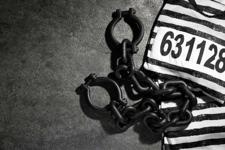 Steel shackles and jail clothes on gray table, flat lay. Space for text