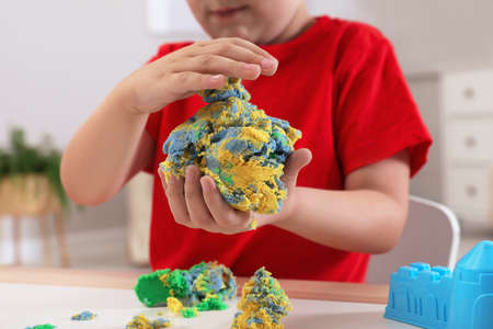 Little boy playing with bright kinetic sand at table in room, closeupの写真素材