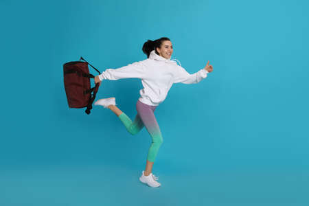 Beautiful woman with sports bag running on light blue backgroundの写真素材