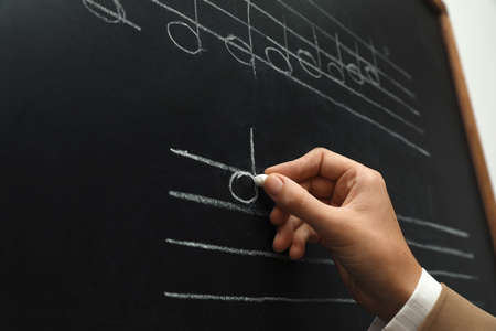 Teacher writing music notes with chalk on blackboard, closeupの写真素材