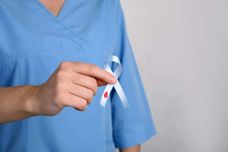 Doctor holding light blue ribbon with paper blood drop on gray background, closeup. World Diabetes Dayの写真素材