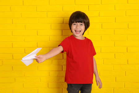 Cute little boy with paper plane near yellow brick wallの写真素材