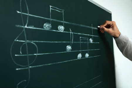 Teacher writing music notes with chalk on greenboard, closeupの写真素材