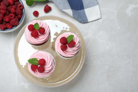 Delicious cupcakes with cream and raspberries on light gray marble table, flat lay. Space for textの写真素材