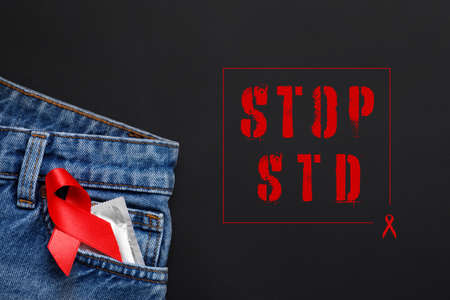 Jeans with condom and red ribbon in pocket on black background, top view. STOP STDの写真素材