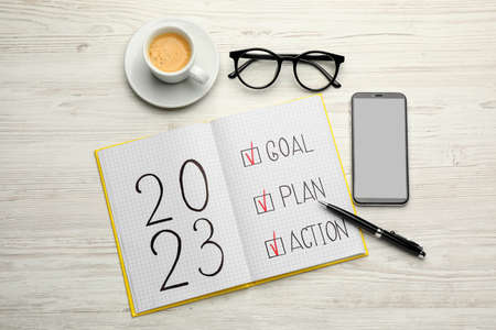 Flat lay composition of notebook with text 2023 Goal, Plan, Action on white wooden table. New year resolutionsの写真素材