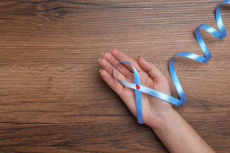 Woman holding light blue ribbon with paper blood drop at wooden table, top view and space for text. Diabetes awarenessの写真素材