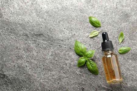 Glass bottle of basil essential oil and leaves on gray stone table, flat lay. Space for textの写真素材