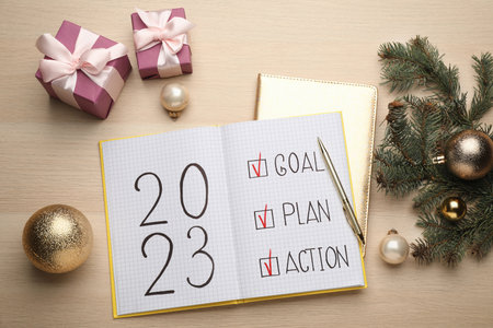 Flat lay composition of notebook with text 2023 Goal, Plan, Action and festive decor on wooden...