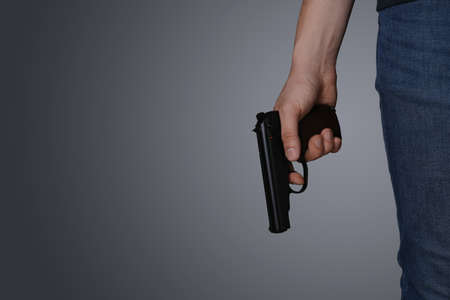 Man holding gun on dark background, closeup. Space for textの写真素材