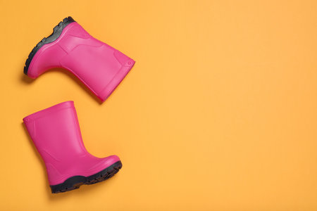 Pair of bright pink rubber boots on orange background, top view. Space for textの写真素材