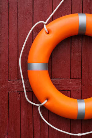 Orange life buoy hanging on red wooden wallの写真素材