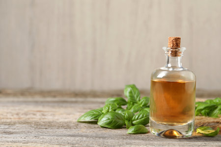 Glass bottle of basil essential oil and leaves on wooden table. Space for textの写真素材
