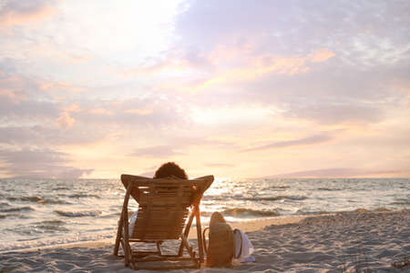 Woman resting in wooden sunbed on tropical beach at sunsetの写真素材