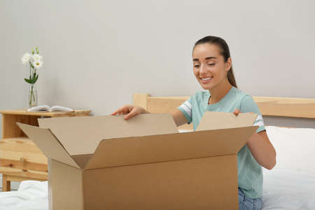 Happy young woman opening parcel on bed at home. Internet shopping