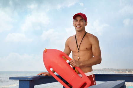 Handsome lifeguard with life buoy on watch tower against skyの写真素材