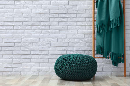 Stylish knitted pouf and ladder with plaid near white brick wall indoors, space for text. Interior designの写真素材