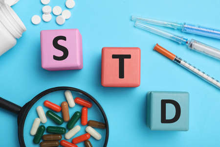 Abbreviation STD made with cubes near different drugs on light blue background, flat layの写真素材
