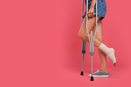 Young woman with injured leg using axillary crutches on pink background, closeup. space for textの写真素材