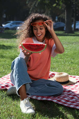 Beautiful young African American woman with slice of watermelon in parkの写真素材