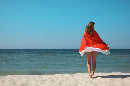 Woman with beach towel near sea on sunny day, back viewの写真素材