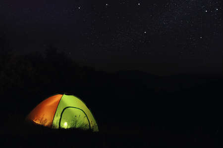 Camping tent glowing at night outdoors. Space for textの写真素材