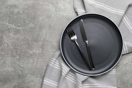 New dark plate with cutlery and napkin on light gray table, top view. Space for textの写真素材