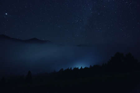 Picturesque view of night sky with beautiful stars over foggy hillの写真素材