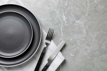 New dark plates, cutlery and napkin on light gray marble table, flat lay. Space for textの写真素材