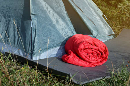 Red sleeping bag near camping tent on green grass outdoorsの写真素材