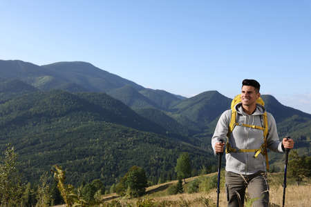 Tourist with backpack and trekking poles hiking through mountains, space for text