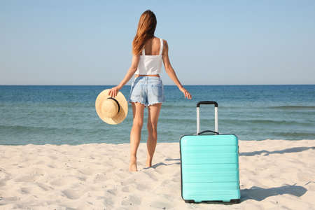 Woman walking to sea and suitcase on beach, back viewの写真素材