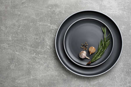New dark plates with rosemary, garlic and peppercorns on light gray table, top view. Space for textの写真素材