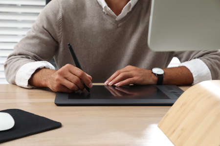 Professional retoucher working on graphic tablet at desk, closeup