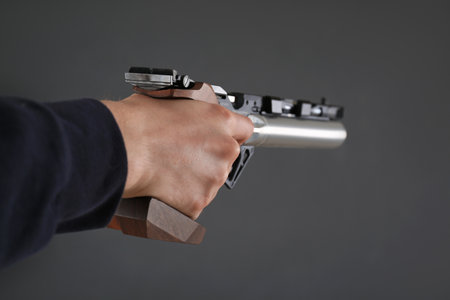 Gun shooting sport. Man aiming standard pistol on dark background, closeup