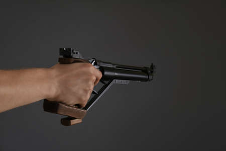 Gun shooting sport. Man aiming standard pistol on dark background, closeup