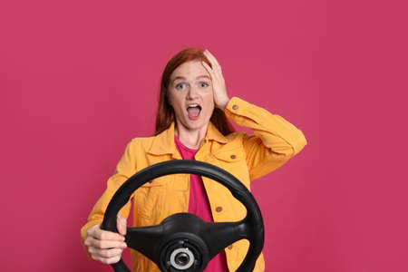 Emotional young woman with steering wheel on crimson backgroundの写真素材