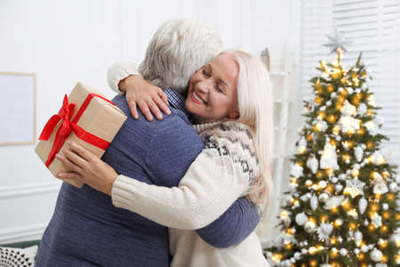 Happy mature couple with gift box hugging at home. Christmas celebrationの写真素材