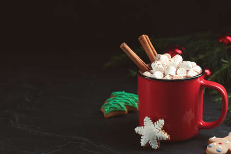 Delicious hot chocolate with marshmallows, cinnamon and gingerbread cookies on black table, space...
