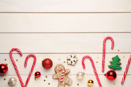 Tasty candy canes, gingerbread cookies and Christmas balls on white wooden table, flat lay. Space...
