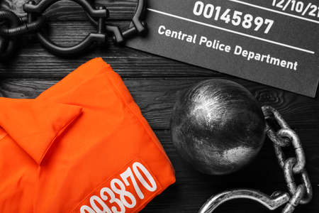 Metal ball with chain, prison uniform and mugshot letter board on black wooden table, flat layの写真素材